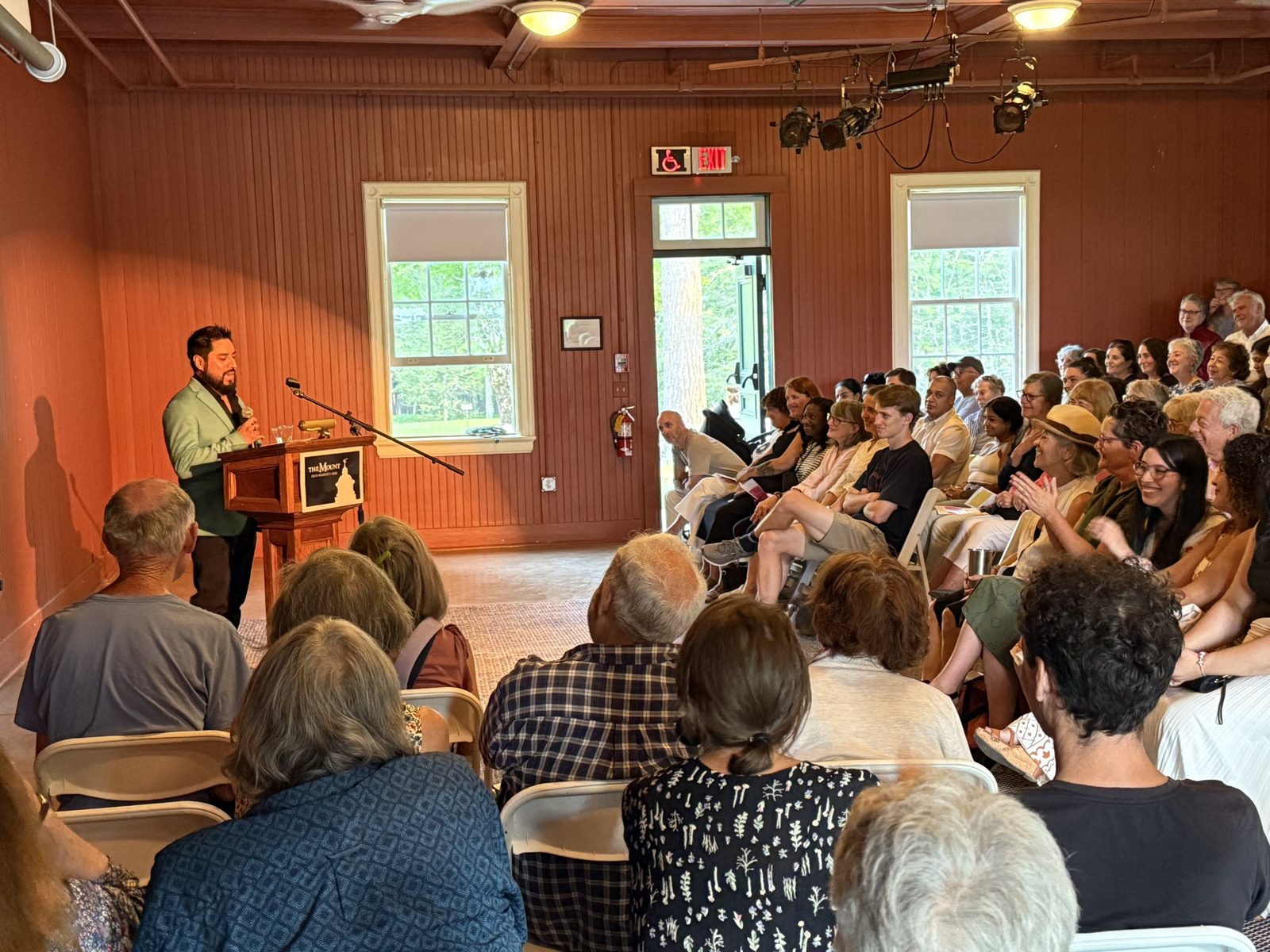 A LitNet storyteller speaks at the podium to a full audience in The Mount’s Stable Auditorium